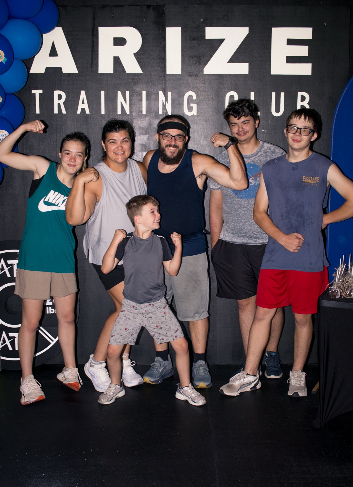 A whole family flexes together beneath the Arize Training Club sign in Yukon, Oklahoma.