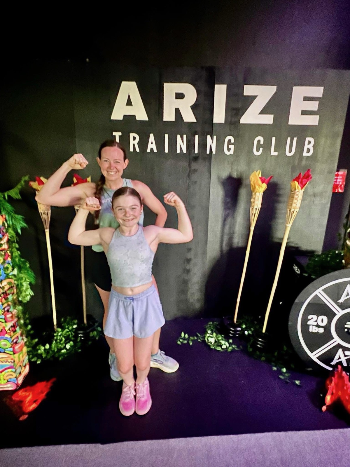 A mother and daughter both flex their arms beneath the Arize Training Club sign in Yukon, Oklahoma.
